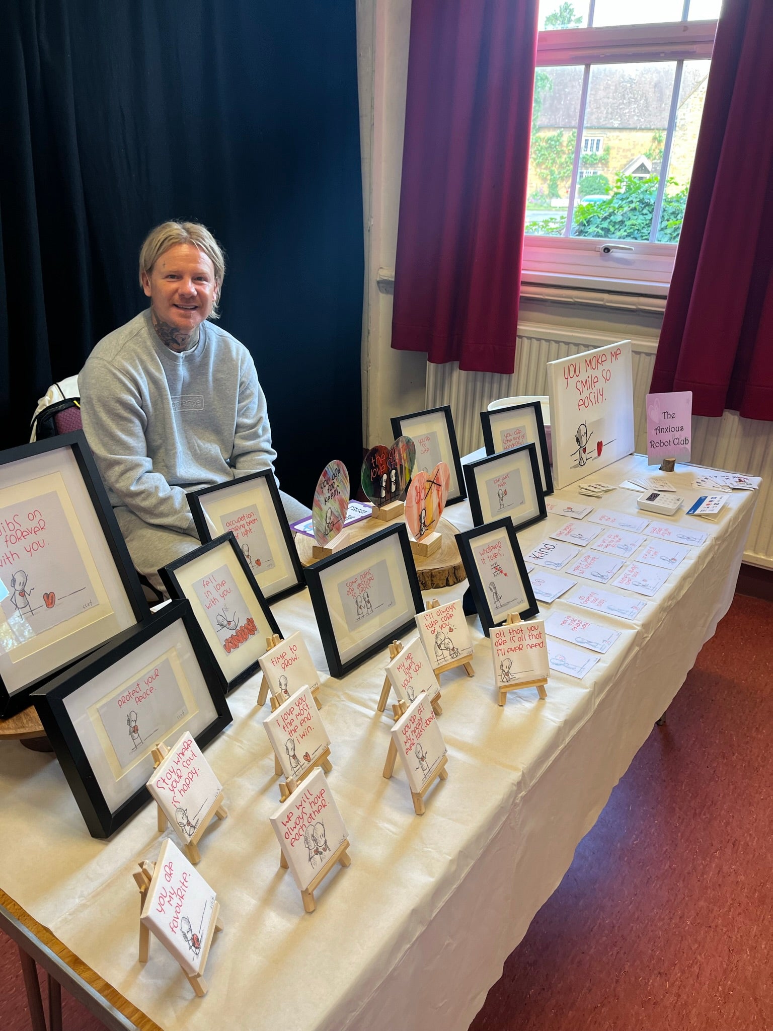 Man sitting behind a table displaying framed artwork and cards.